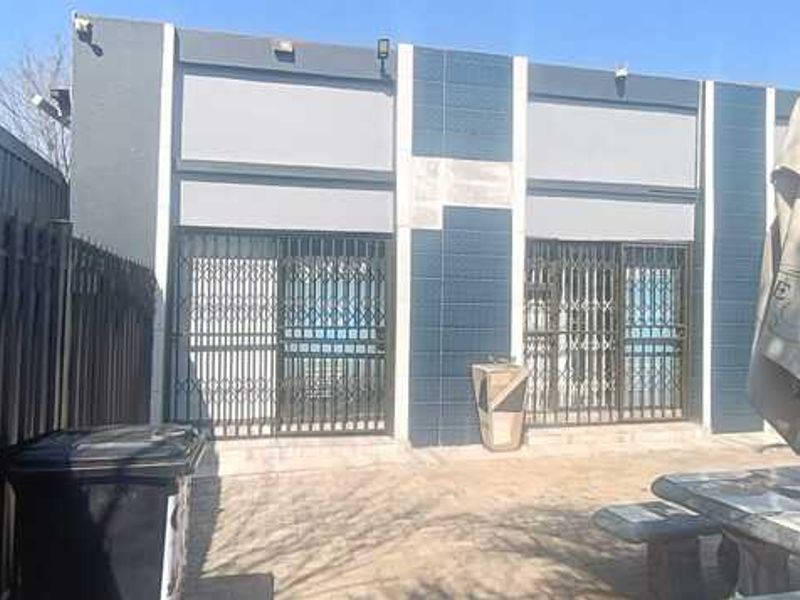 Rear exterior view of the business property featuring a paved patio area, security gates, and modern dark-toned facade finishes.