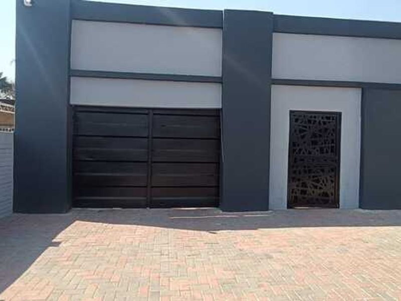 Modern commercial exterior facade featuring a paved driveway, secure black metal gate, and decorative laser-cut metal entrance door.