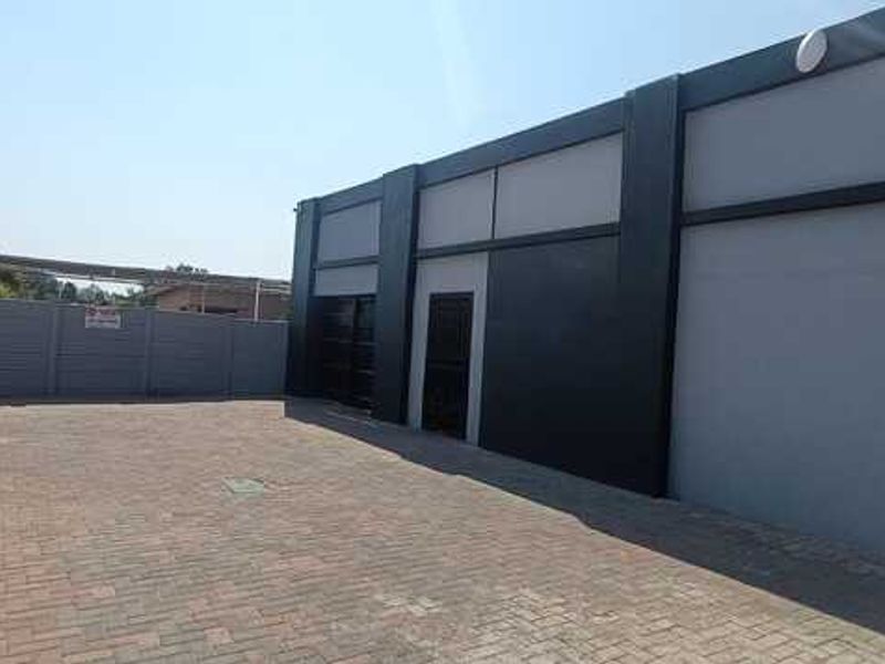 A modern commercial exterior featuring a paved parking area, secure perimeter wall, and a contemporary building facade with dark accent detailing.