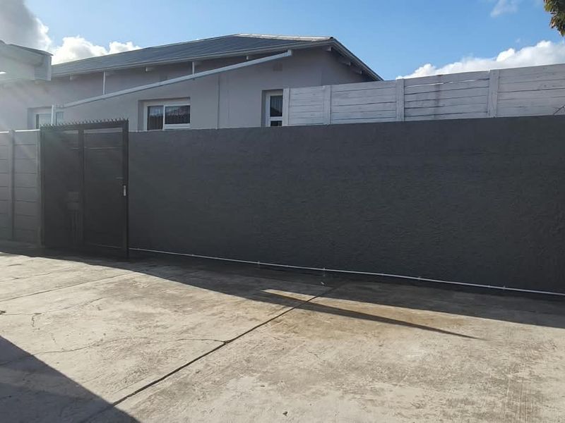 A paved rear courtyard area featuring a dark-painted boundary wall, metal gate, and access to the building via a sliding door.