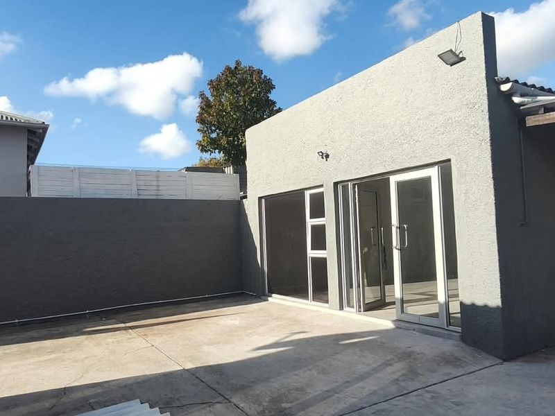 Rear exterior view of the office building featuring a concrete patio area, boundary wall, and sliding glass door access.