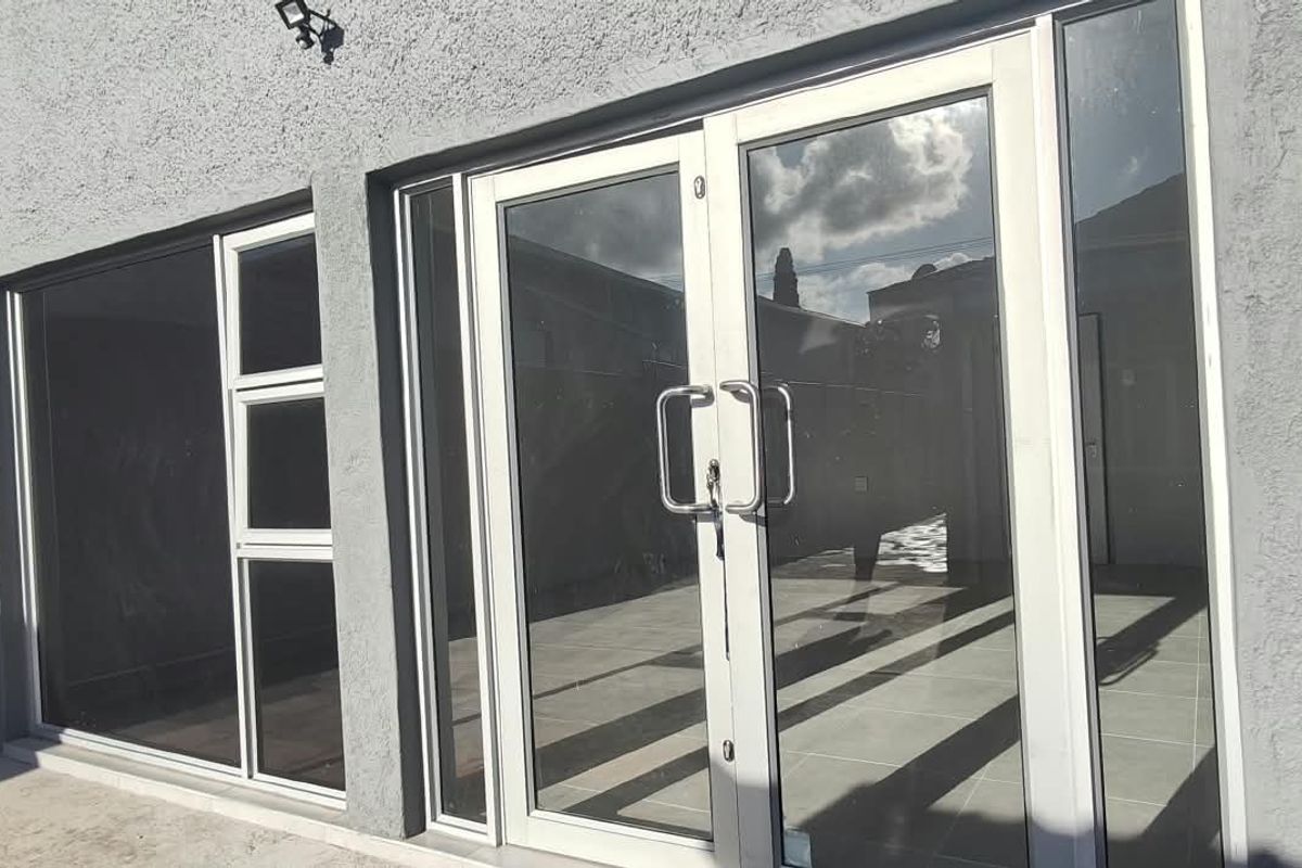 Rear exterior view of the office building featuring modern aluminium-framed glass double doors and large windows opening onto a tiled patio area.