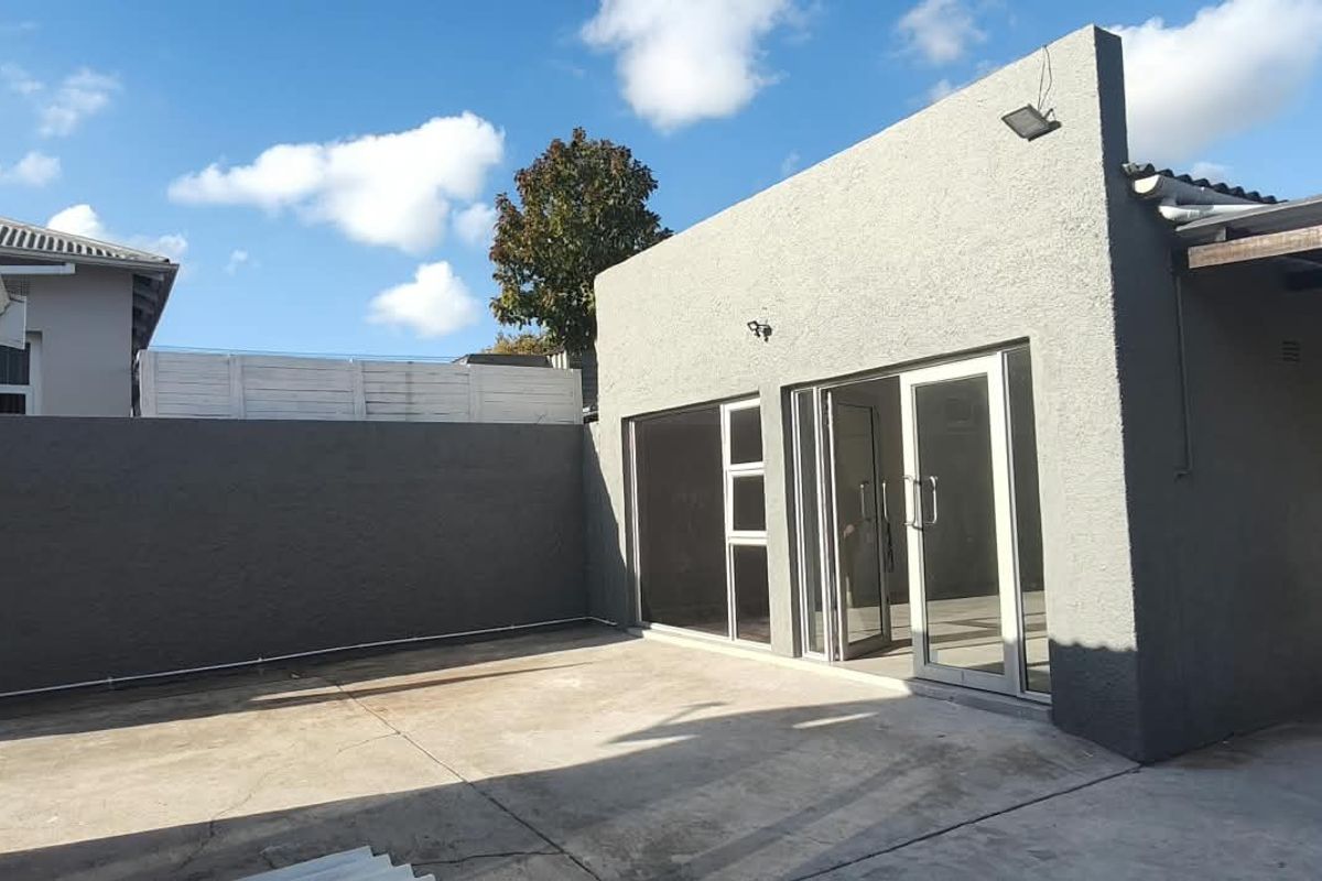 Rear exterior view of the office building featuring a concrete patio area, boundary wall, and sliding glass door access.