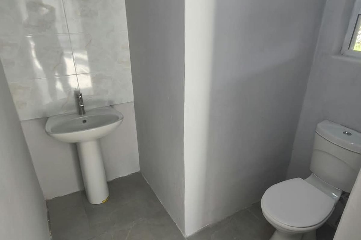 A clean and functional bathroom featuring a pedestal sink with tiled splashback, a standard toilet, and tiled flooring.