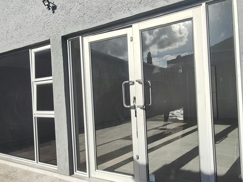 Rear exterior view of the office building featuring modern aluminium-framed glass double doors and large windows opening onto a tiled patio area.