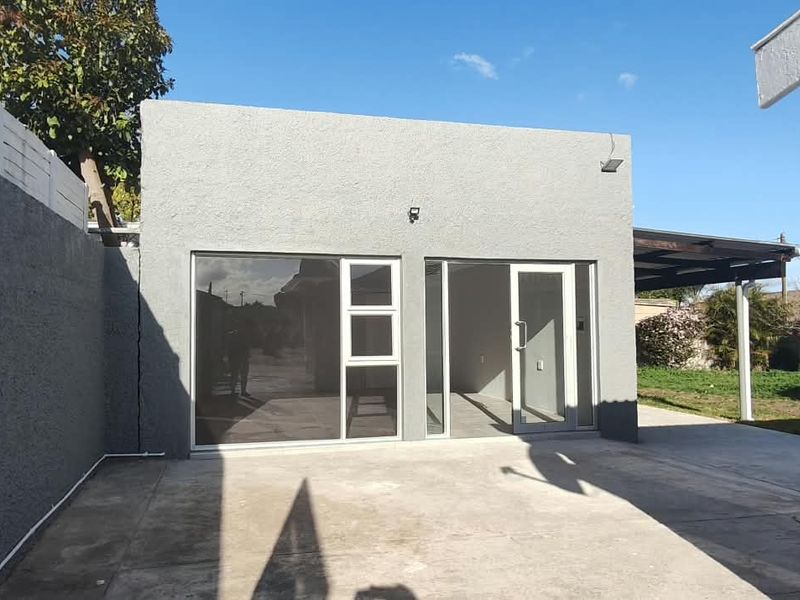 Rear view of the office building featuring a concrete patio, sliding glass doors, and a surrounding boundary wall.