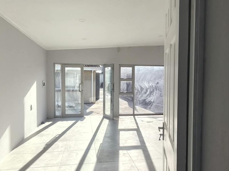 A bright, empty office space featuring neutral tiled flooring and large aluminium-framed glass doors providing natural light and access to the exterior.