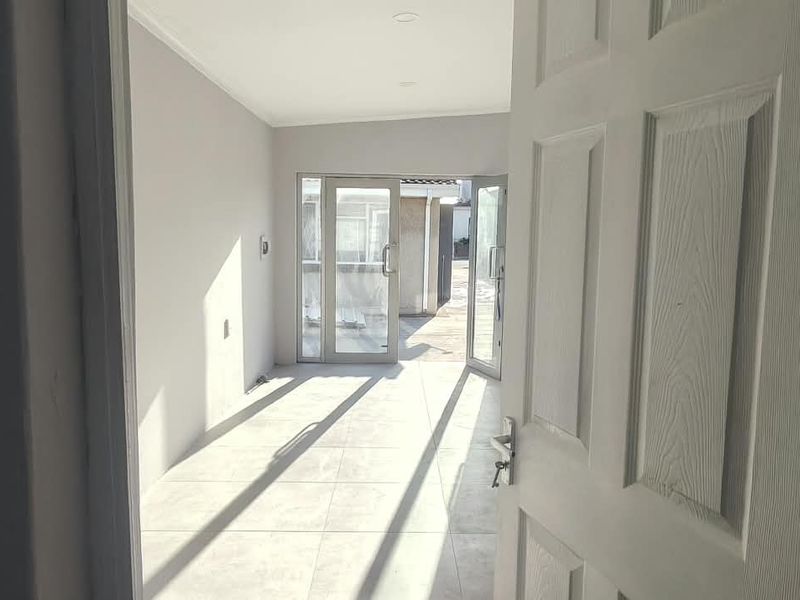 A bright, empty office space featuring neutral tiled flooring and glass sliding doors providing access to an outdoor area.