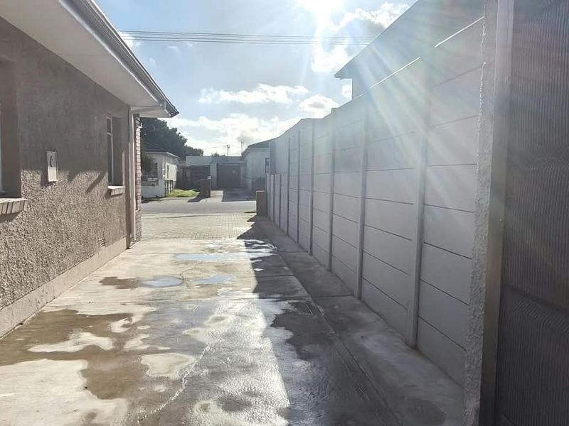 A side exterior view of the office property featuring a concrete driveway, precast boundary wall, and aluminium window frames with security bars.