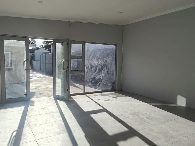 A bright, empty office space featuring large aluminium-framed glass doors, neutral grey walls, and modern tiled flooring, offering a clean and versatile workspace.