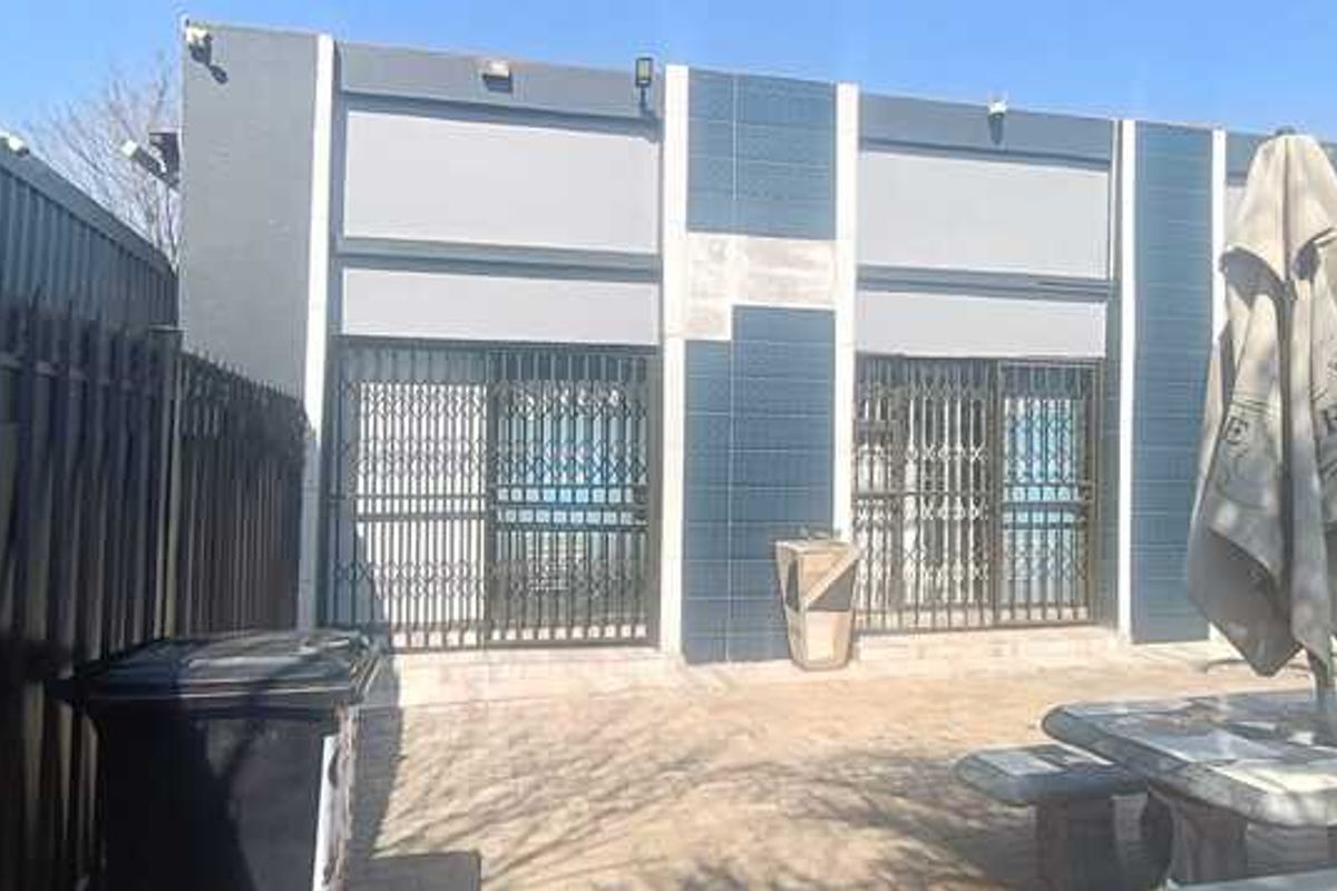 Rear exterior view of the business property featuring a paved patio area, security gates, and modern dark-toned facade finishes.