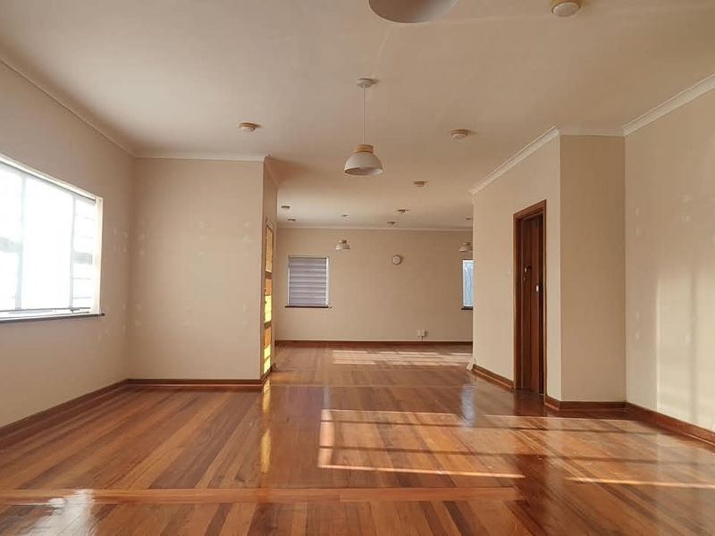 Spacious open-plan office area featuring polished hardwood flooring, neutral walls with recent patching, and multiple pendant light fixtures throughout the interior space.