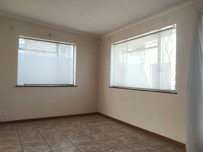 A vacant office space featuring tiled flooring, neutral walls, and large windows with security bars, offering a clean canvas for professional use.