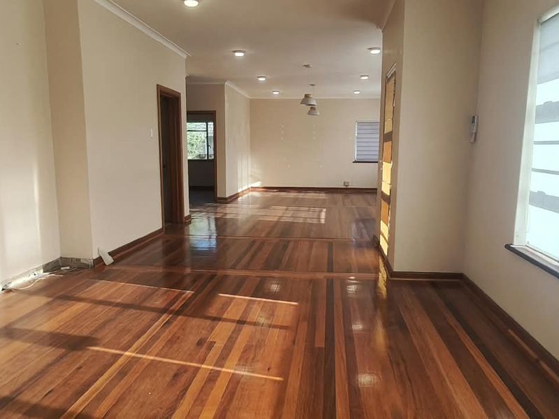 Spacious open-plan office area featuring polished hardwood flooring, recessed lighting, and large windows providing ample natural light.