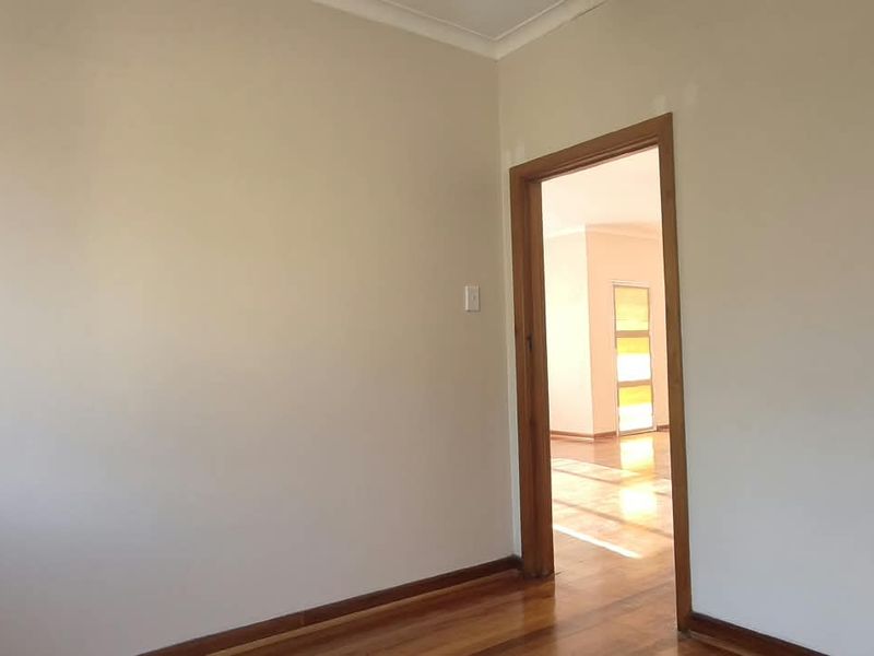 A vacant office space featuring polished timber flooring and a timber door frame leading to an adjacent room.