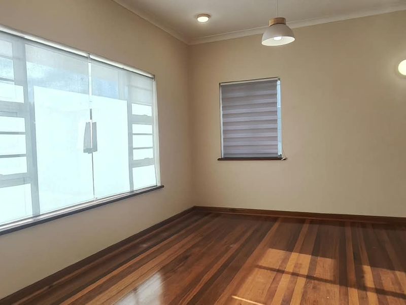 A bright, empty office space featuring polished hardwood flooring, large windows with fitted roller blinds, and modern lighting fixtures.