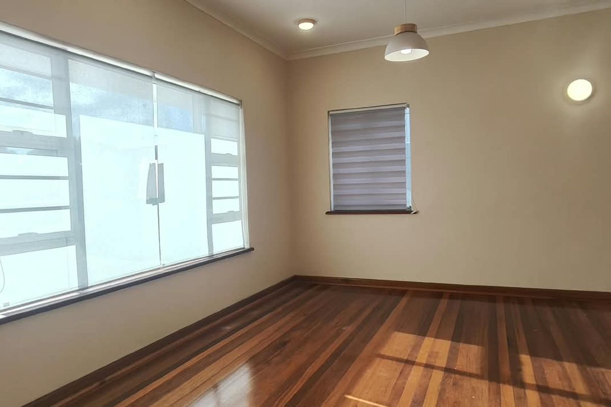 A bright, empty office space featuring polished hardwood flooring, large windows with fitted roller blinds, and modern lighting fixtures.