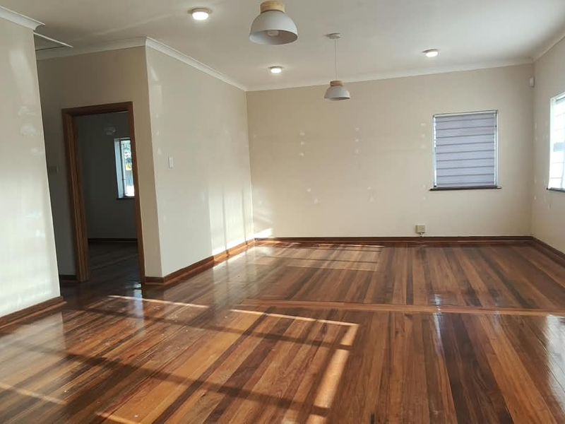 A spacious, empty office area featuring polished hardwood flooring, recessed and pendant lighting, and neutral walls with visible patching ready for final paint.