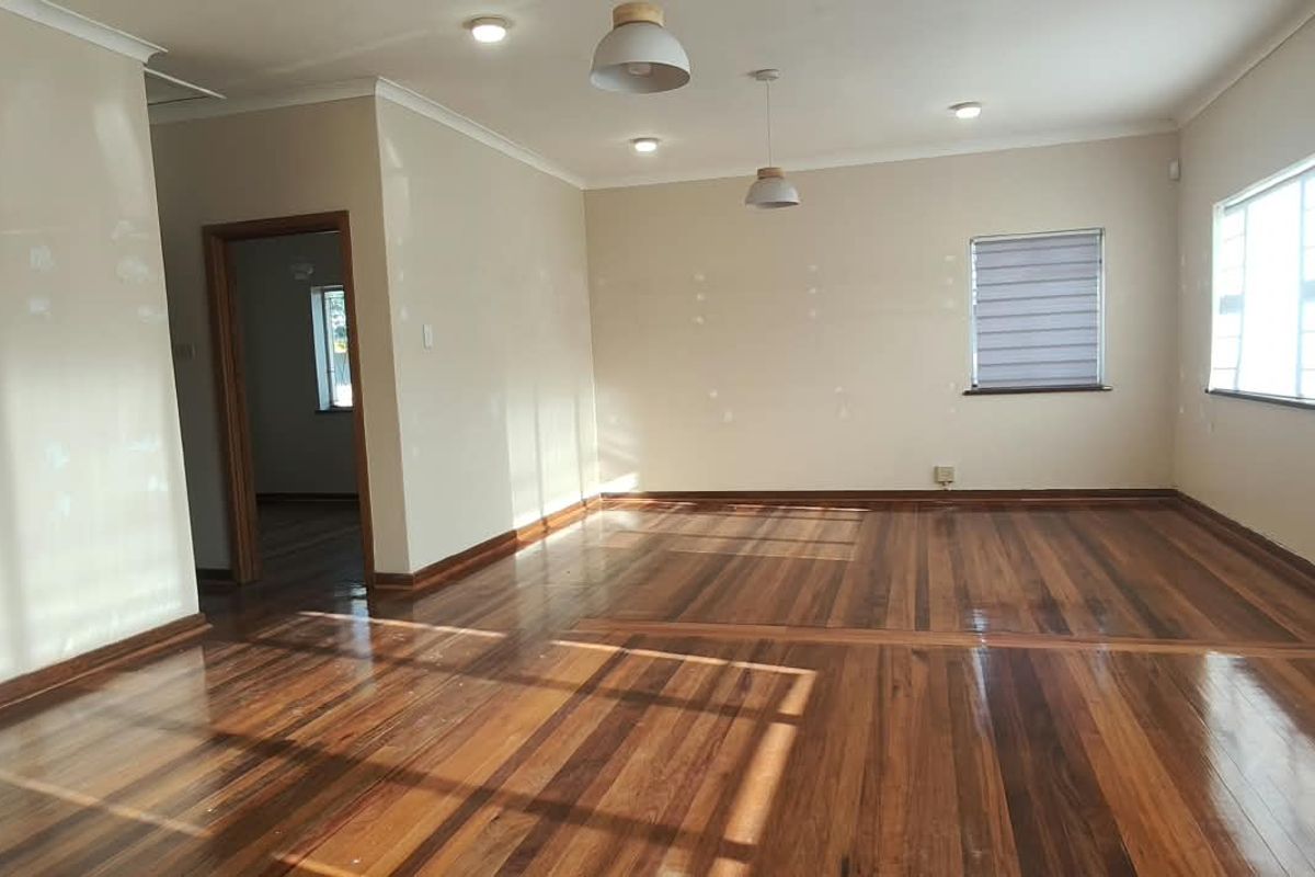 A spacious, empty office area featuring polished hardwood flooring, recessed and pendant lighting, and neutral walls with visible patching ready for final paint.