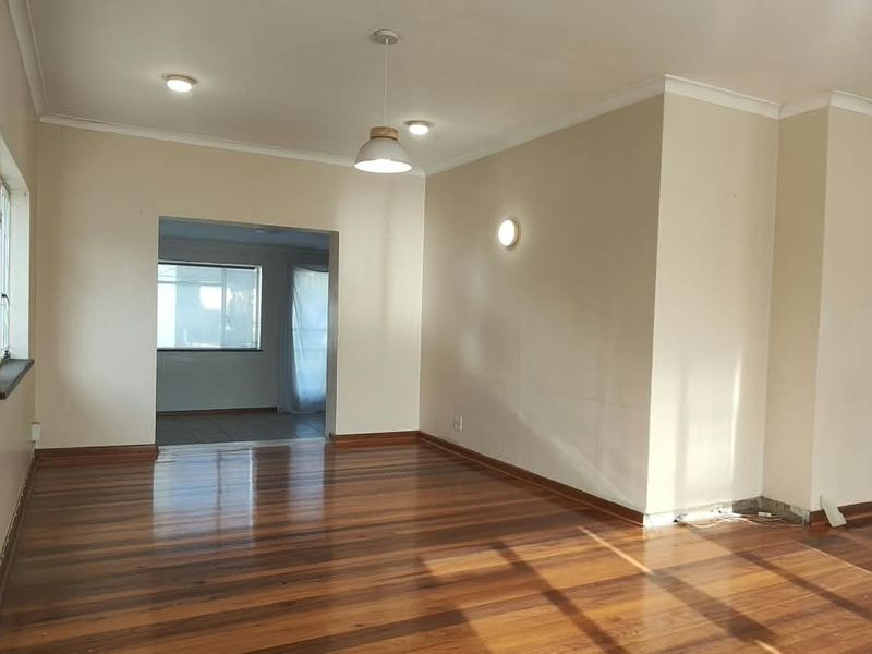 Spacious, empty office area featuring polished hardwood flooring, recessed lighting, and neutral wall finishes, offering a versatile workspace layout.