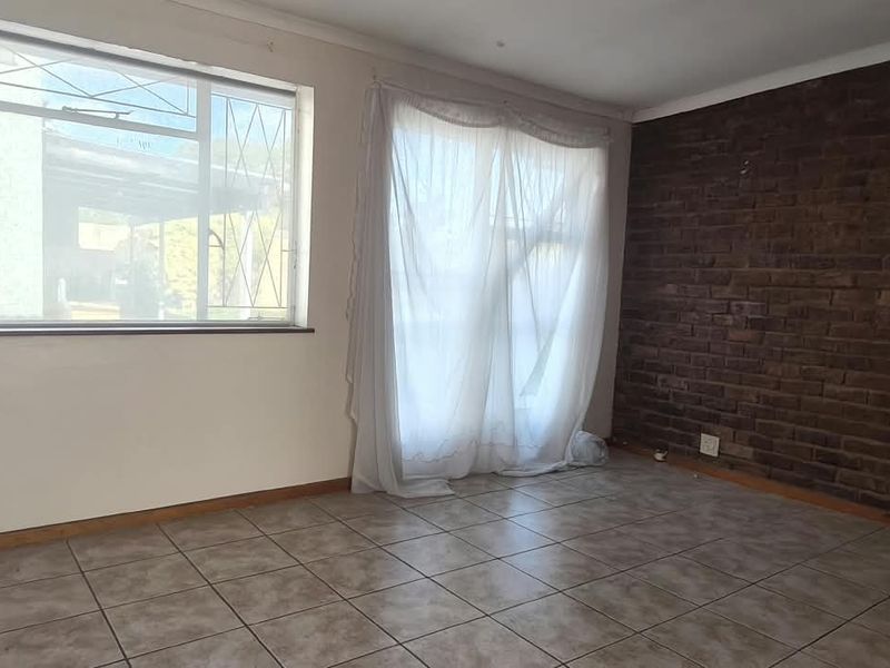 An empty office space featuring tiled flooring, an exposed brick feature wall, and large windows with security bars.