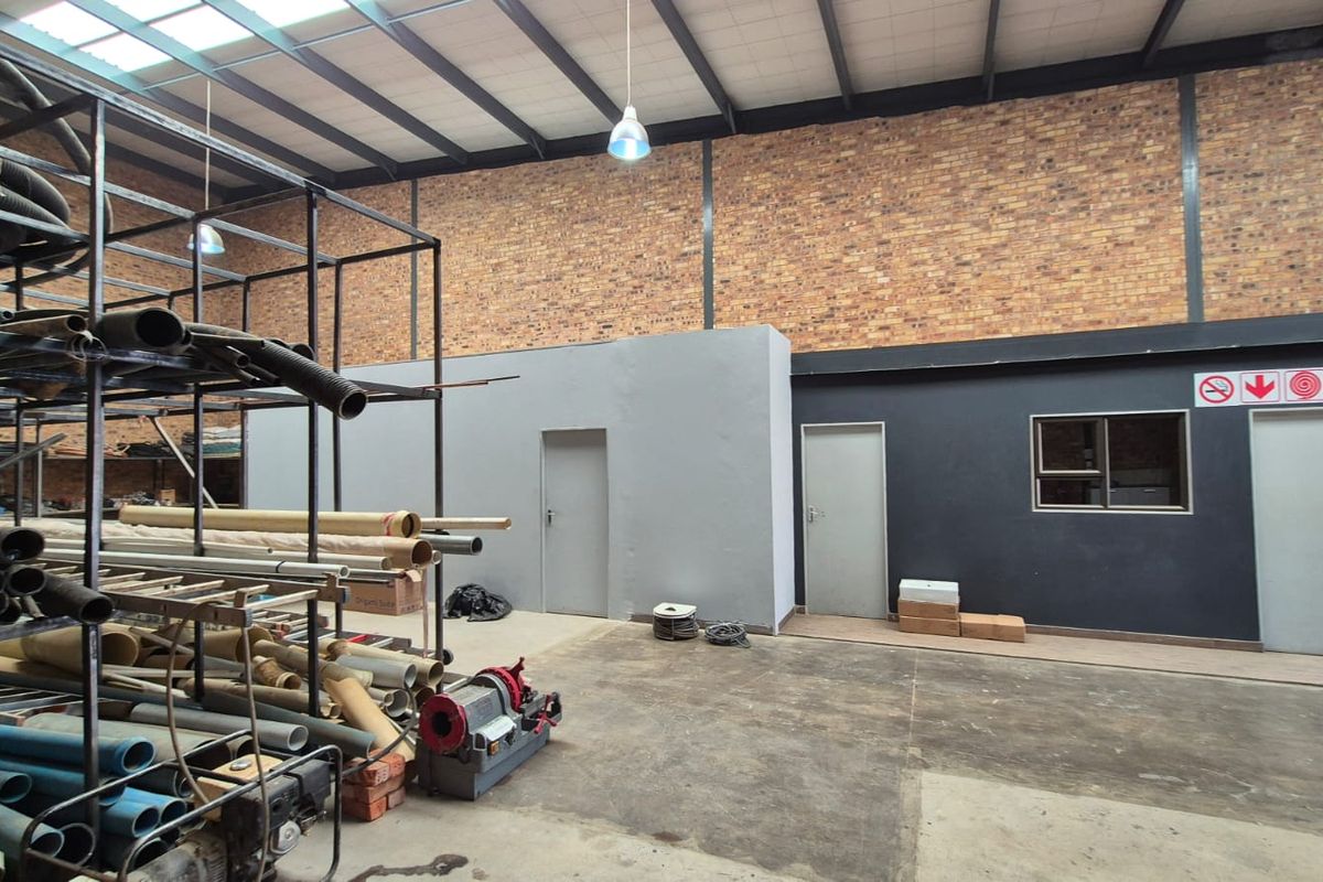 Spacious industrial utility area featuring exposed brick walls, high ceilings with steel trusses, concrete flooring, and multiple access points.
