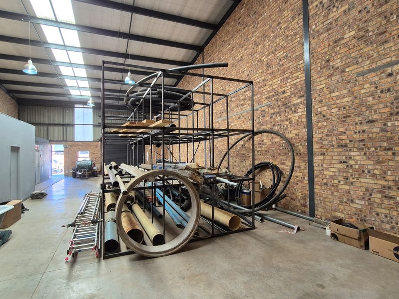 Spacious industrial utility area featuring exposed brick walls, high ceilings with skylights, and durable concrete flooring, suitable for storage or workshop use.