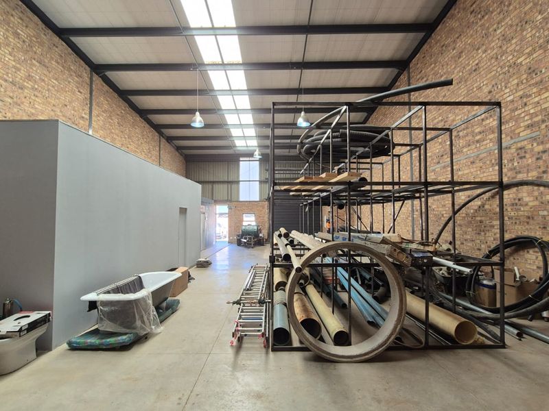 Spacious industrial utility area featuring exposed brick walls, high steel portal frame ceiling with skylights, and durable concrete flooring.