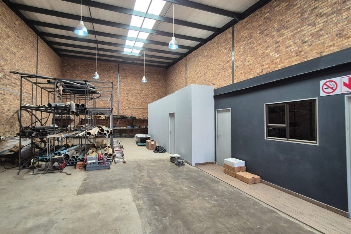 Spacious industrial utility area featuring exposed brick walls, high ceilings with steel trusses, skylights, and a dedicated internal office partition.