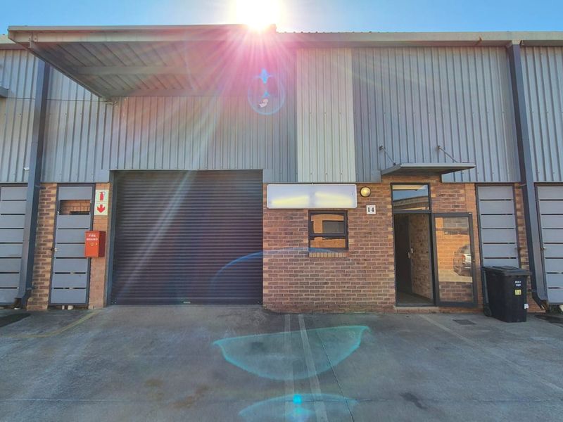 Front elevation of an industrial unit featuring a roller shutter door, brick and metal cladding facade, and a concrete driveway entrance.