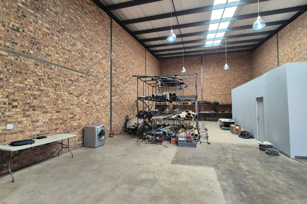 Spacious industrial utility area featuring exposed brick walls, high steel truss ceilings with skylights, and durable concrete flooring, suitable for storage or workshop use.