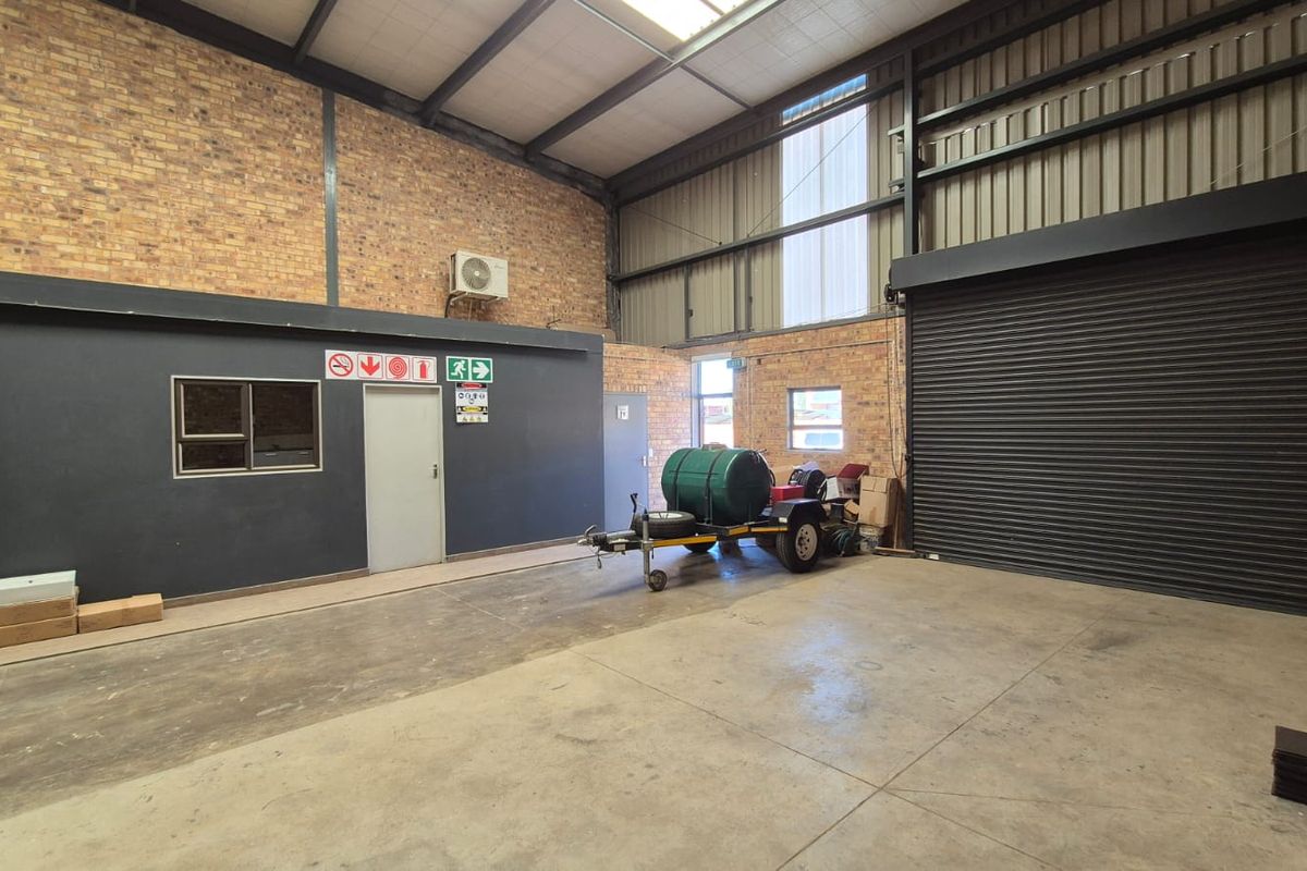 Spacious industrial utility area featuring exposed brick walls, high ceilings with steel trusses, concrete flooring, and a large roller shutter door for easy access.