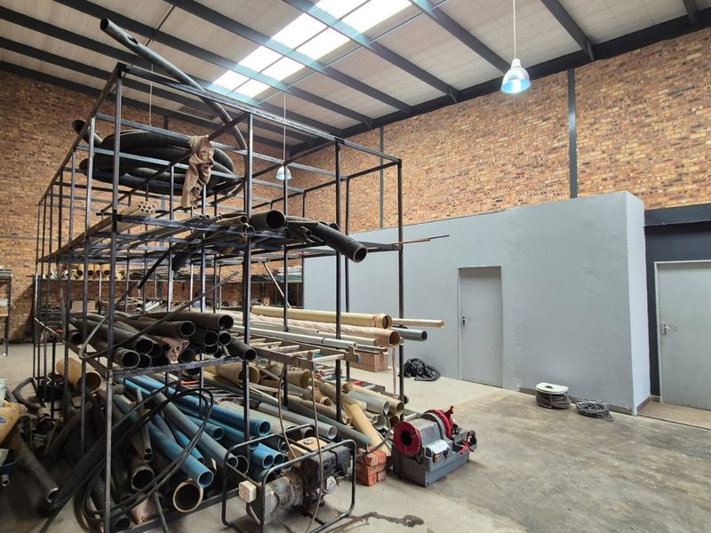 Spacious industrial utility area featuring exposed brick walls, high steel truss ceilings with skylights, and durable concrete flooring.