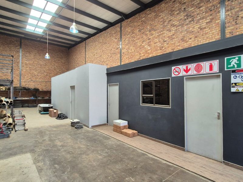 Spacious industrial utility area featuring exposed brick walls, high steel truss ceilings with skylights, and durable concrete flooring, suitable for storage or workshop use.