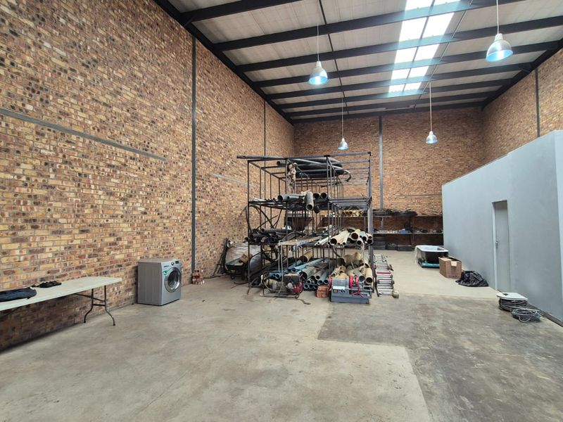 Spacious industrial utility area featuring exposed brick walls, high steel truss ceilings with skylights, and durable concrete flooring, suitable for storage or workshop use.