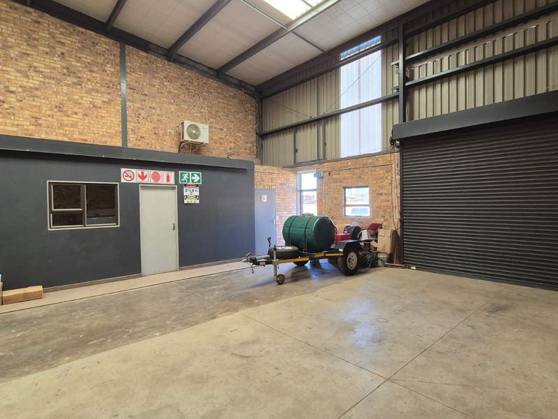 Spacious industrial utility area featuring exposed brick walls, high ceilings with steel trusses, concrete flooring, and a large roller shutter door for easy access.