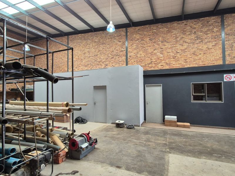 Spacious industrial utility area featuring exposed brick walls, high ceilings with steel trusses, concrete flooring, and multiple access points.