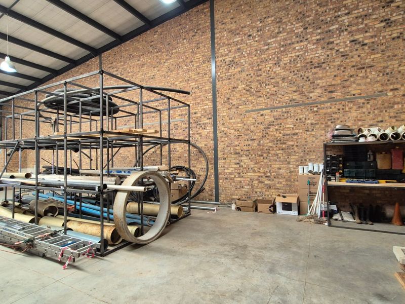 Spacious industrial utility area featuring exposed brick walls, high-bay lighting, and durable concrete flooring, suitable for storage or workshop operations.