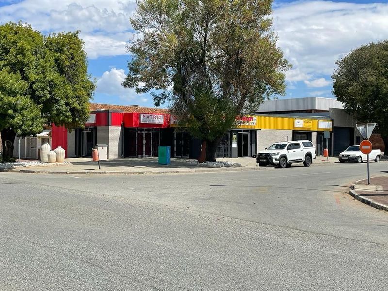 Street-level view of a commercial property featuring multiple storefronts with metal security gates and signage.