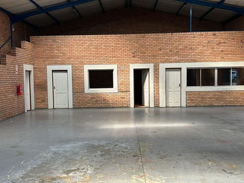 Spacious industrial warehouse interior featuring exposed brick walls, concrete flooring, multiple access doors, and high-clearance steel roof trusses.