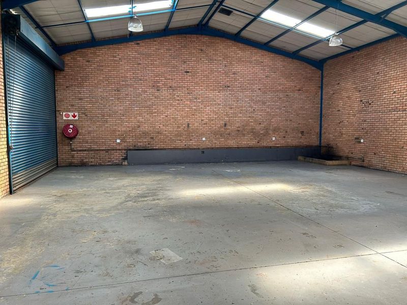 Spacious industrial warehouse unit featuring high ceilings, exposed brick walls, concrete flooring, and a large roller shutter door for easy access.