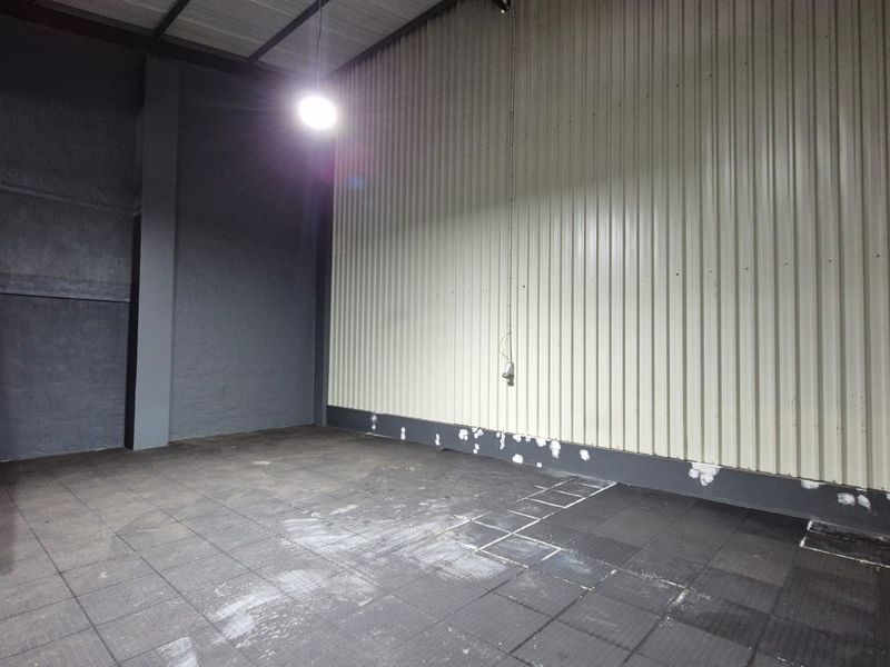 An empty industrial utility space featuring a metal staircase, corrugated wall cladding, and tiled flooring, suitable for storage or workshop use.