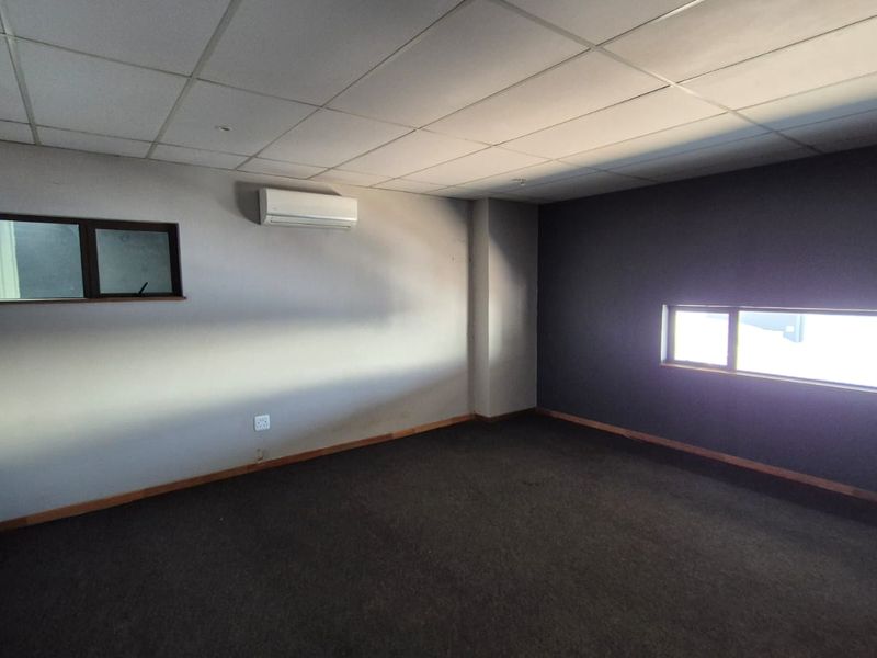 A vacant office space featuring dark carpeting, a suspended ceiling, and a wall-mounted split-system air conditioning unit.