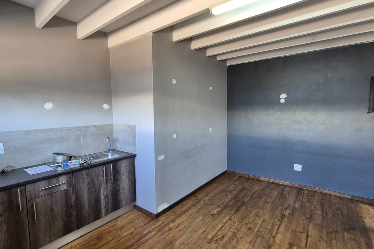 A compact kitchen area featuring built-in cabinetry, a stainless steel sink, laminate flooring, and exposed ceiling beams, currently requiring minor wall finishing.