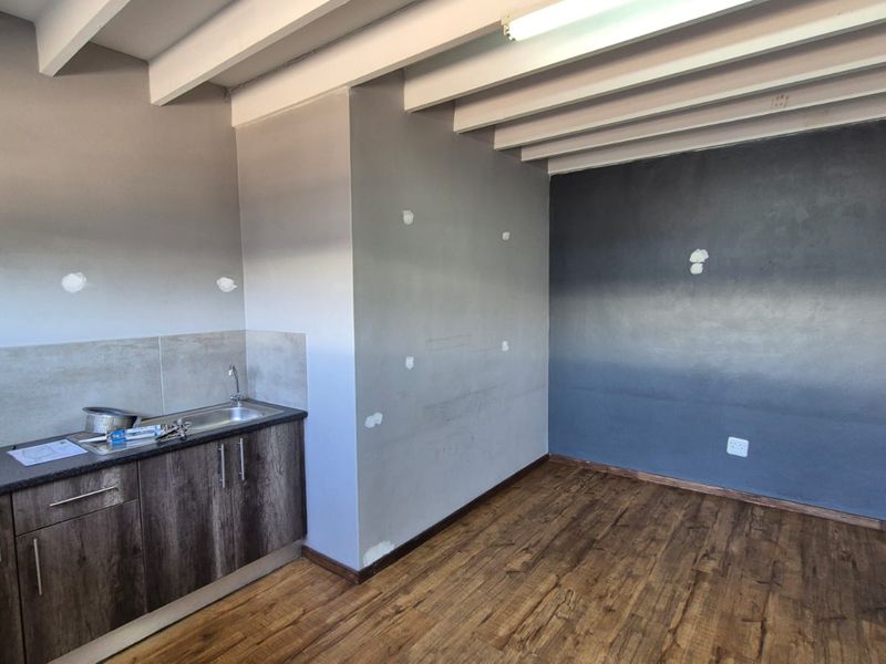 A compact kitchen area featuring built-in cabinetry, a stainless steel sink, laminate flooring, and exposed ceiling beams, currently requiring minor wall finishing.