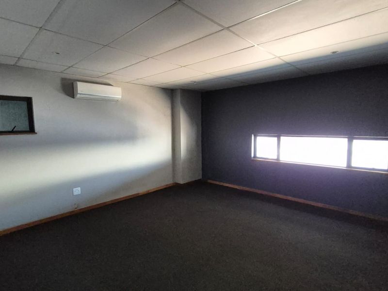 An empty office space featuring a suspended ceiling, carpeted flooring, and a wall-mounted split-system air conditioning unit.