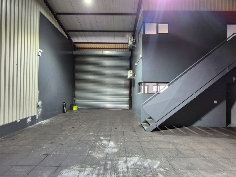 Spacious industrial utility area featuring a large roller shutter door, tiled flooring, and an internal staircase leading to an upper level.