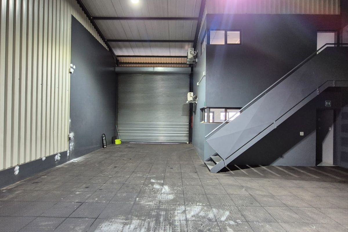 Spacious industrial utility area featuring a large roller shutter door, tiled flooring, and an internal staircase leading to an upper level.