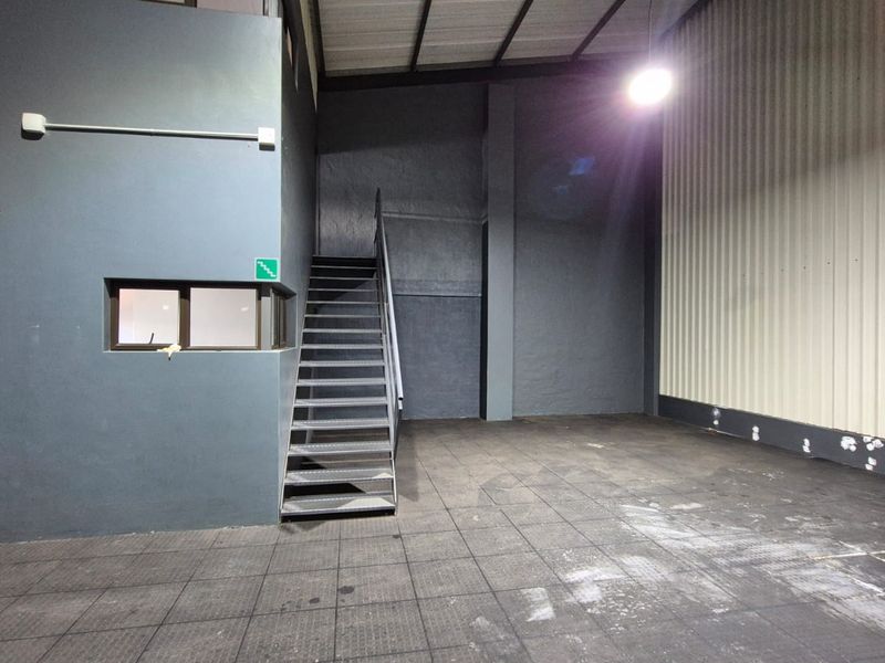 An industrial utility space featuring a metal staircase, tiled flooring, and corrugated metal wall cladding, suitable for storage or workshop use.