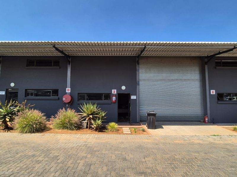 Front elevation of an industrial warehouse unit featuring a large roller shutter door, metal roofing, and paved exterior access area.
